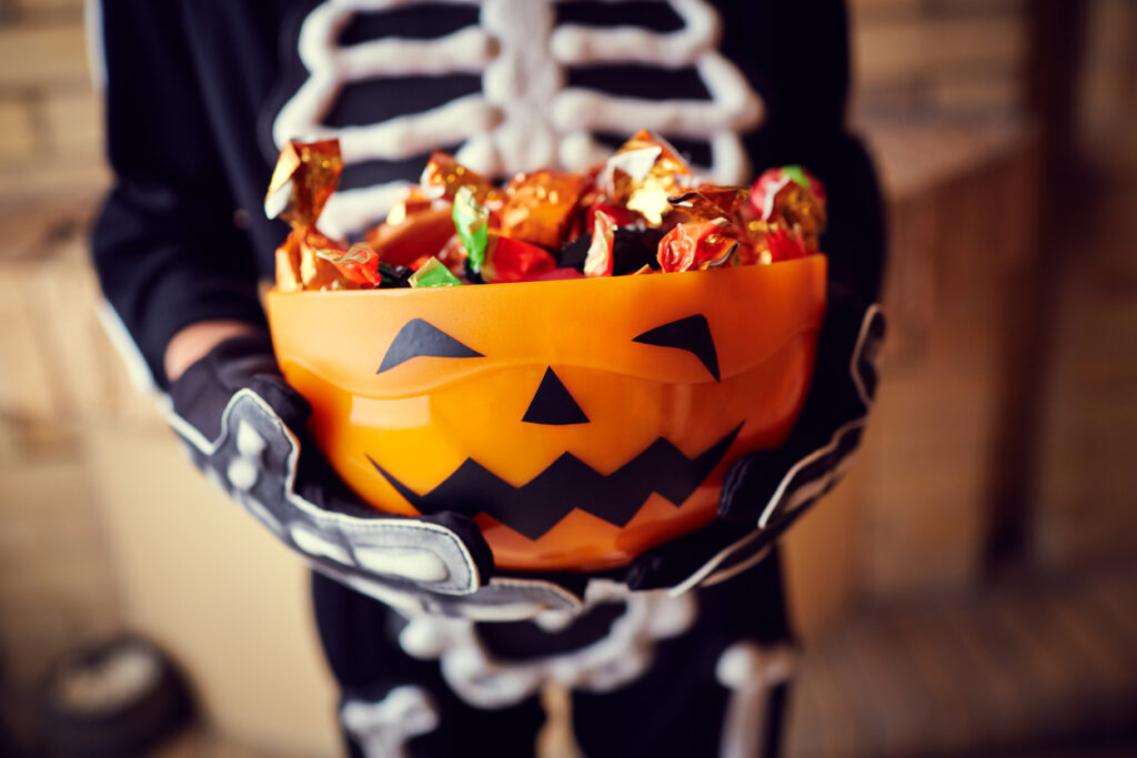 Boy in skeleton costume holding orange bowl of Halloween candy