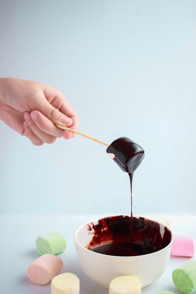 hand dipping colored marshmallow on skewer into melted chocolate