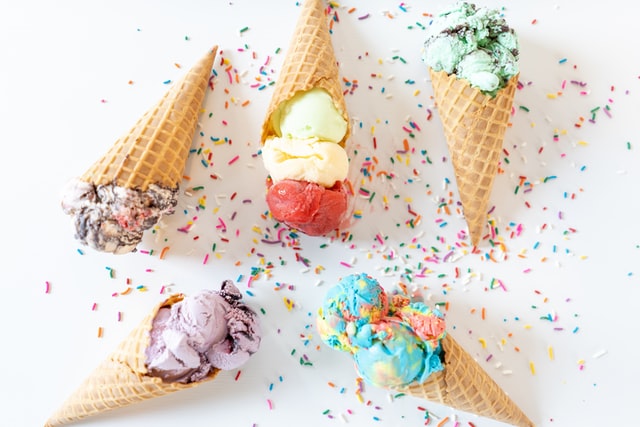 arrangement of five cones filled with different ice cream flavors, surrounded by sprinkles